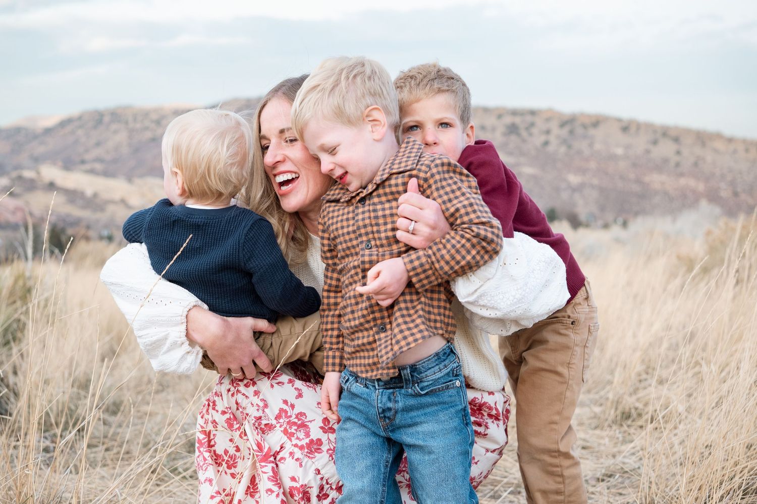 Color portrait of mother kneeling to ground to hug all three of her young sons.