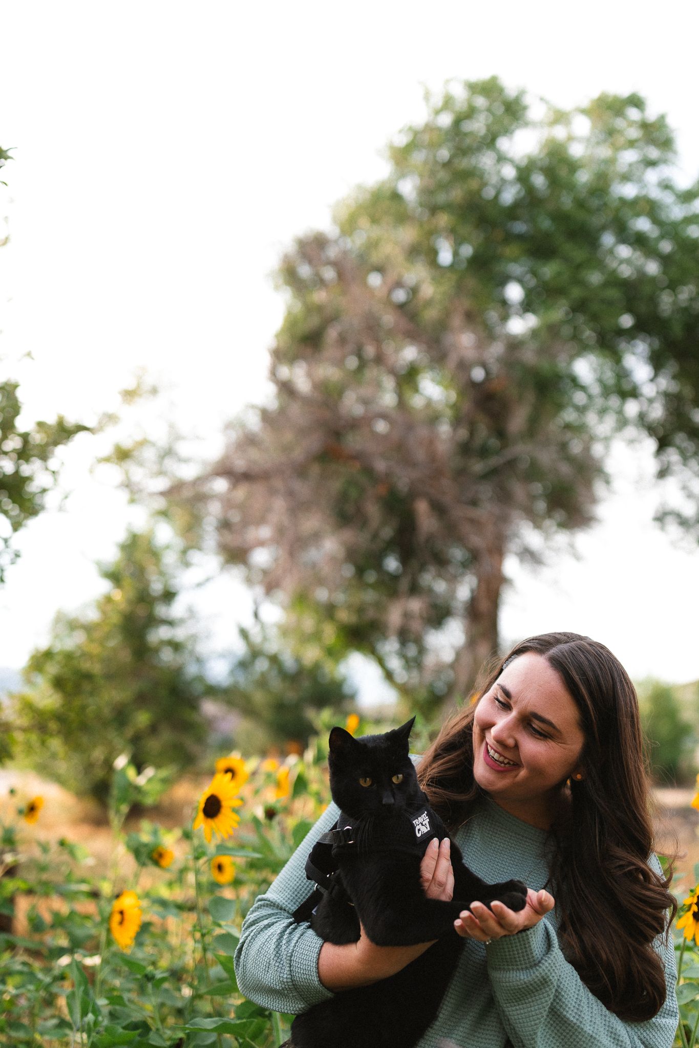 Portrait of Maggie, of Maggie Theis Photography, in her garden, holding her black cat.