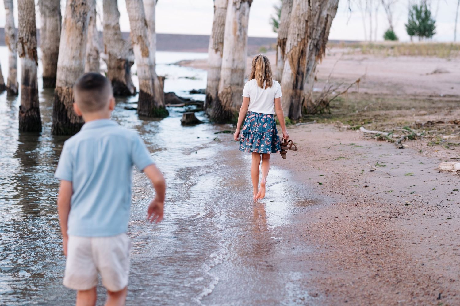 Family photo session at Chatfield State Park, brother and sister walking down shoreline, trees in background.