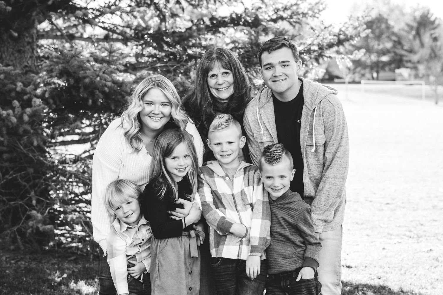 Grandmother standing with two adult grandchildren and four young grandchildren, all smiling.