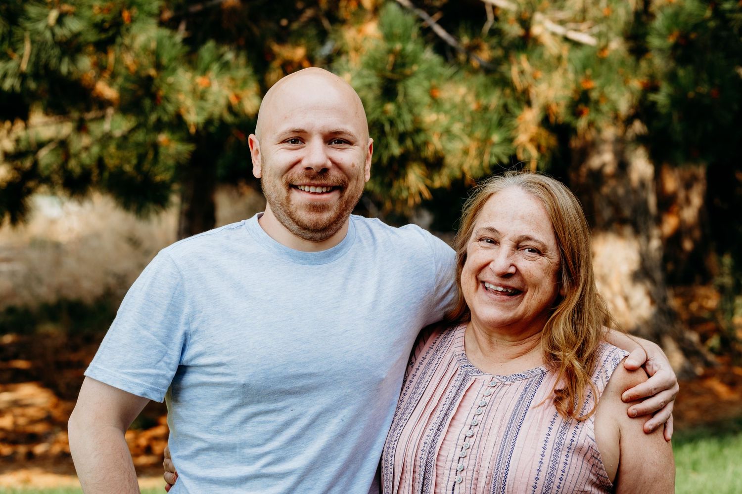 Adult son smiling with mother, trees in background.