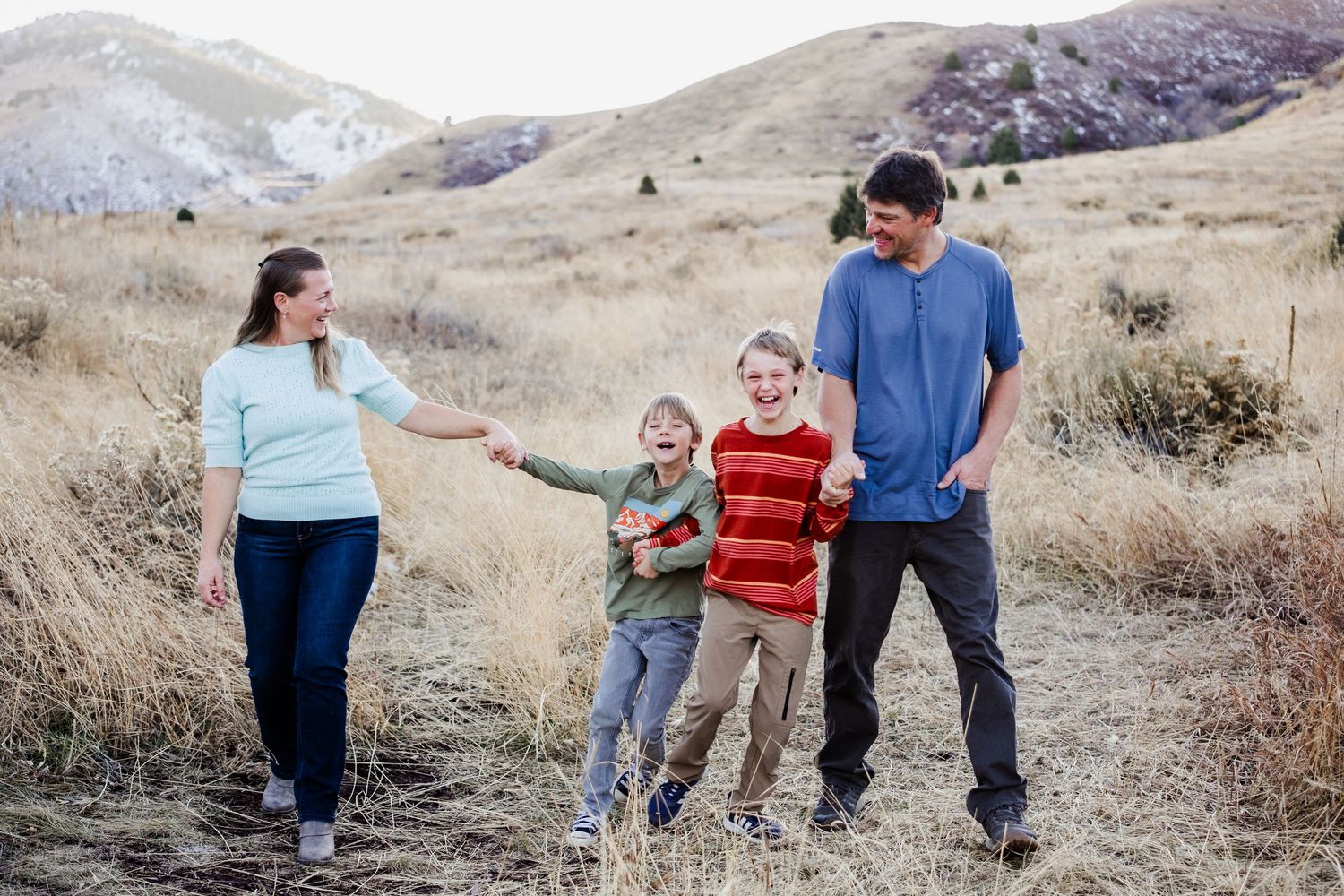 Golden Colorado family photographer captures a laughing family walking on path by warm grasses and foothill views at Matthews / Winter Park.