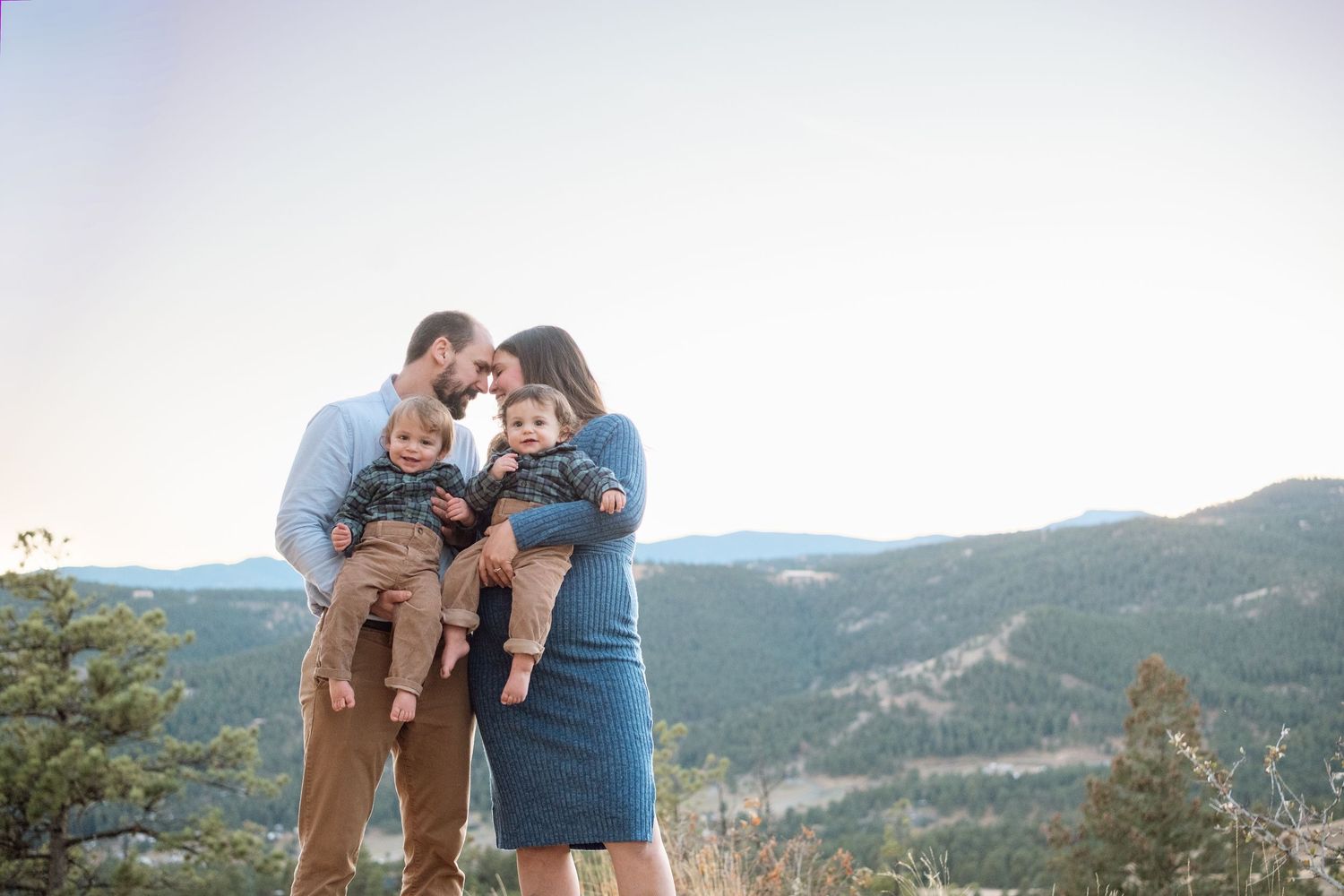 Mother and father, each holding a twin, pressing foreheads together, stunning mountain scene in the background at Mt Falcon West.