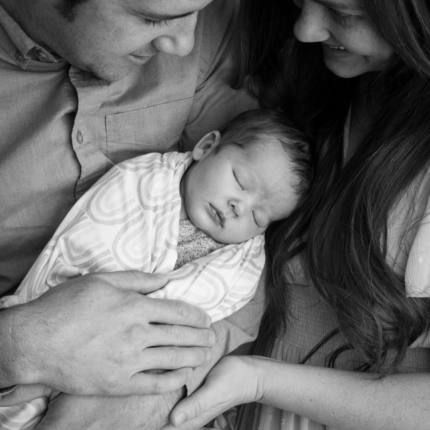 Mother and father snuggled closely together, father holding peacefully sleeping baby boy.