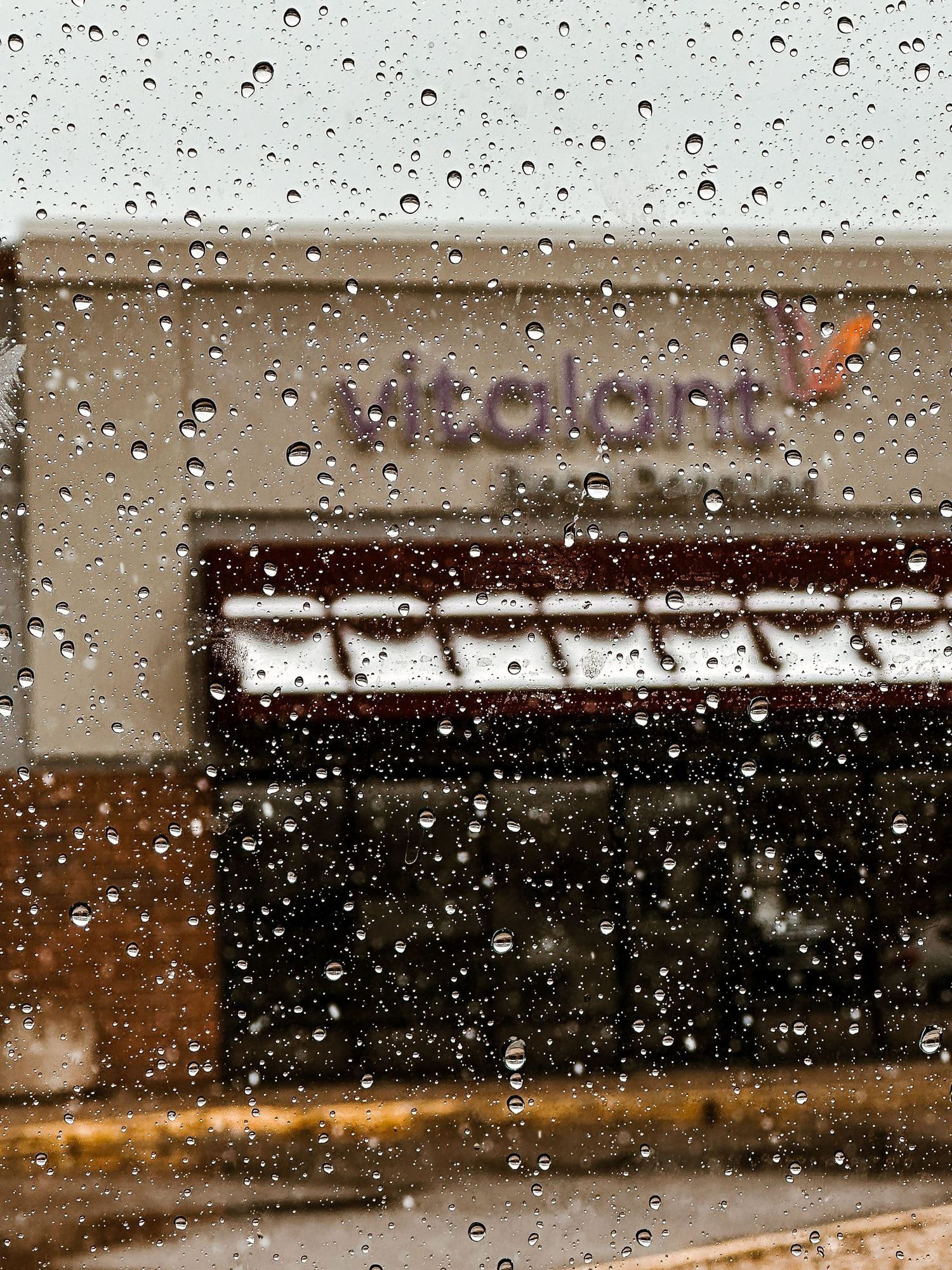 Water droplets on car window, Vitalant building in background.