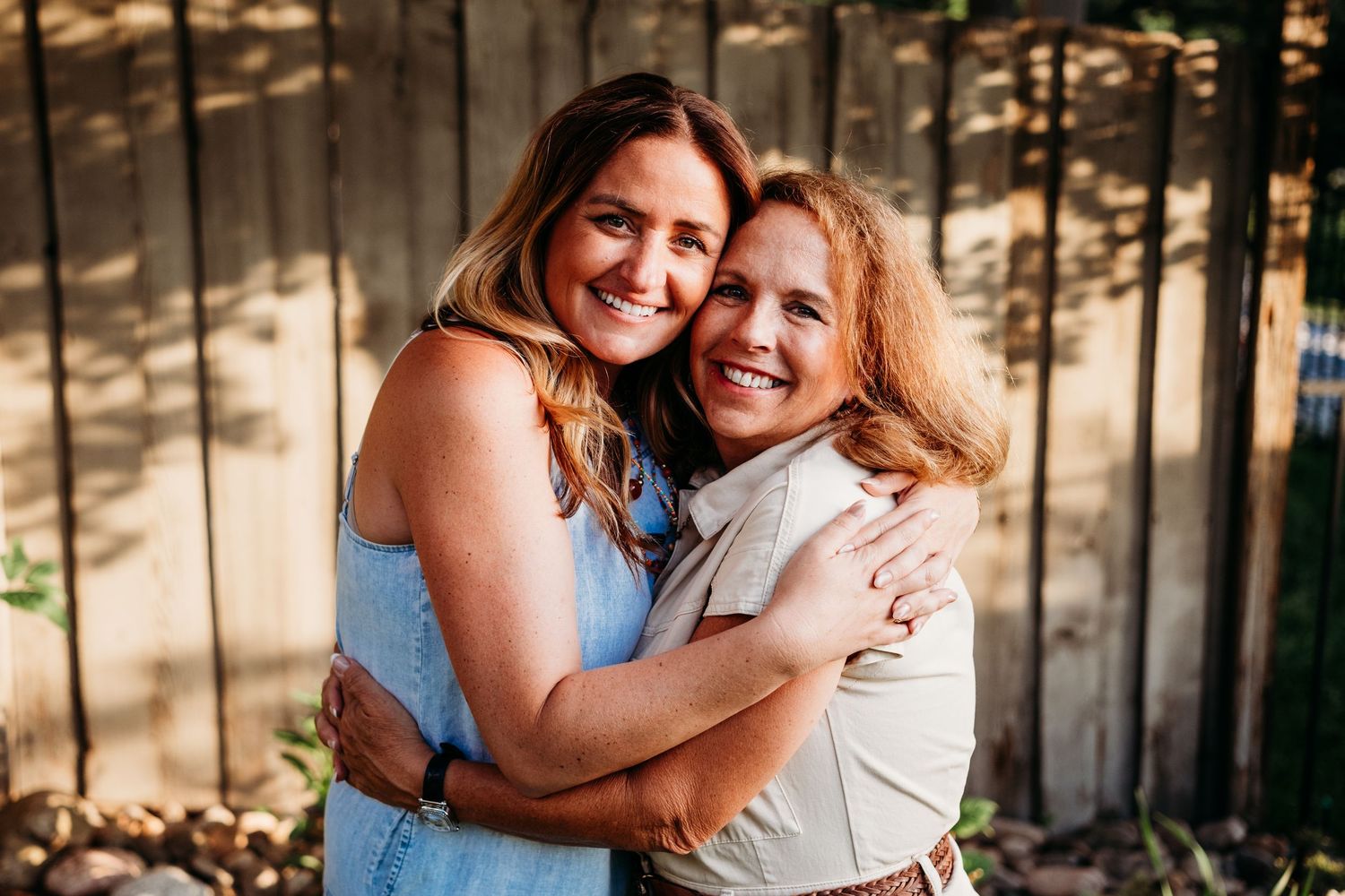 Woman embracing her mother, backyard fence in background, both smiling.