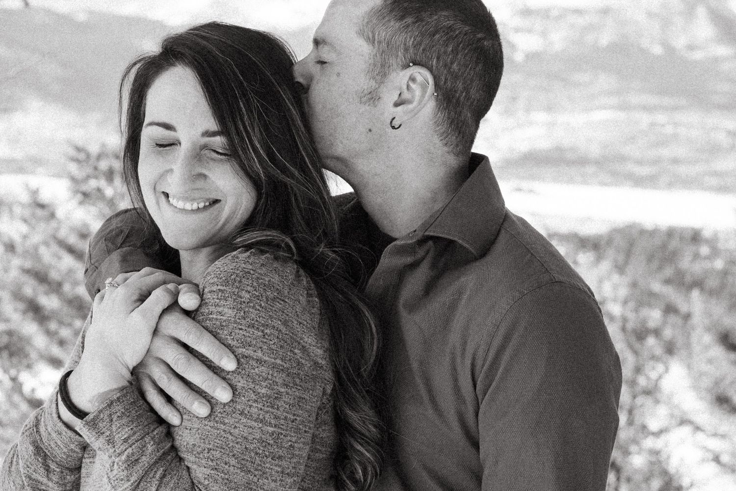 Playful black and white portrait of newly engaged couple, man kissing woman's forehead, at Sapphire Point Overlook.