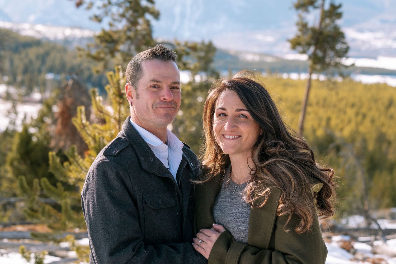 Couple posing and smiling at the camera, evergreen trees and snowcapped mountains in background near Dillon, Colorado.