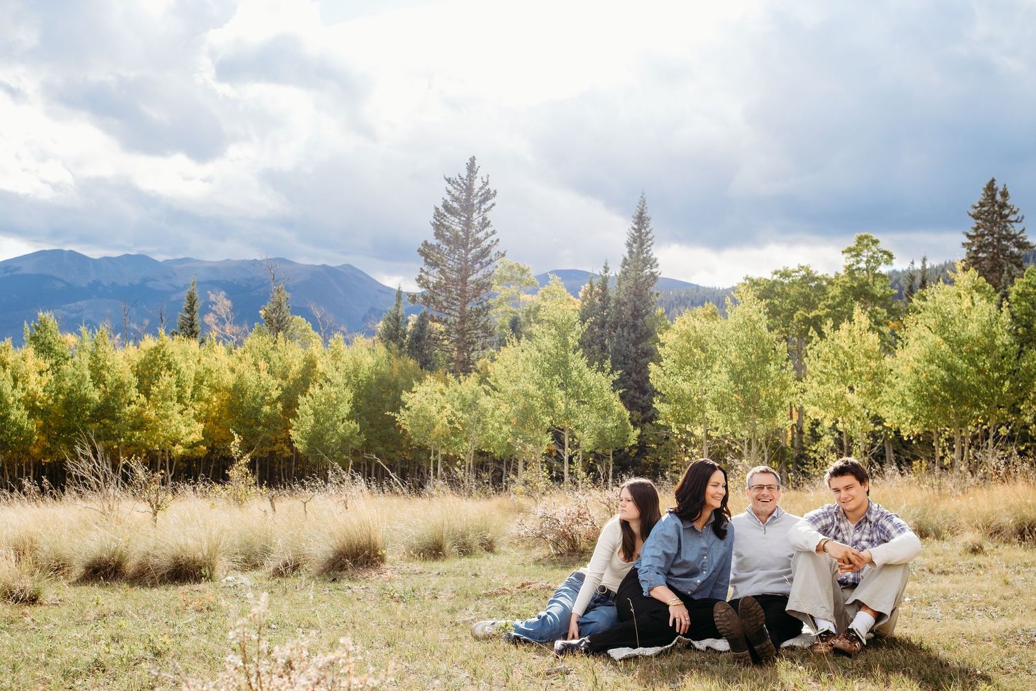 Family with teenagers in Colorado mountains, evergreens, aspens, mountains and moody skies in background.