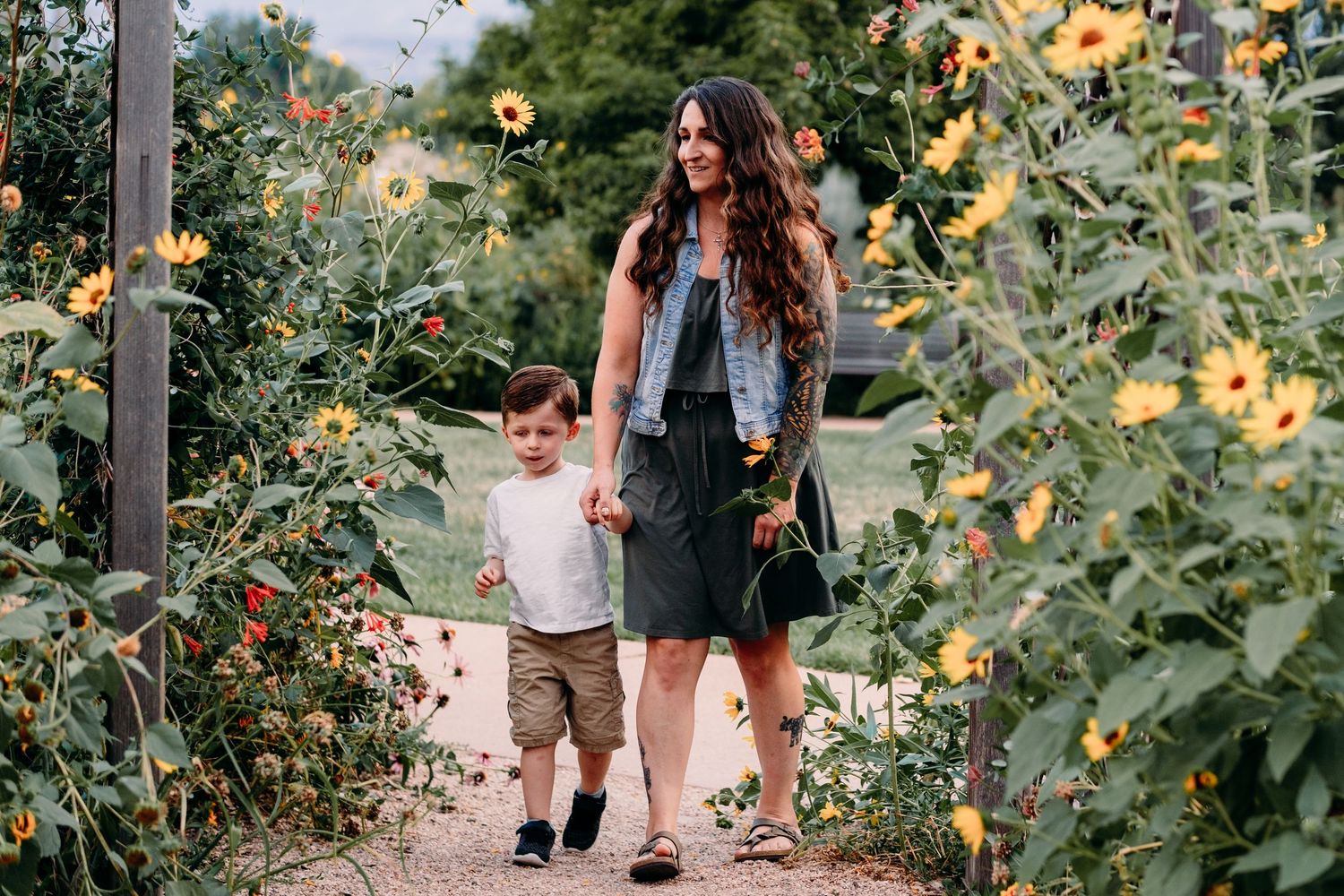 Mother and son walking between sunflowers, holding hands.