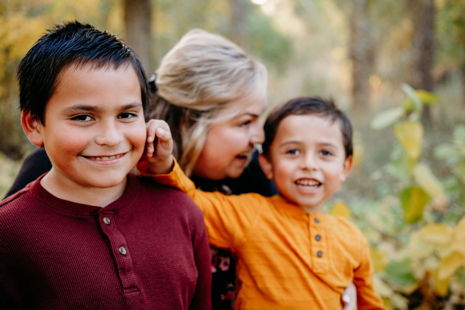 Mother whispering into child's ear as brother playfully pokes at big brother.