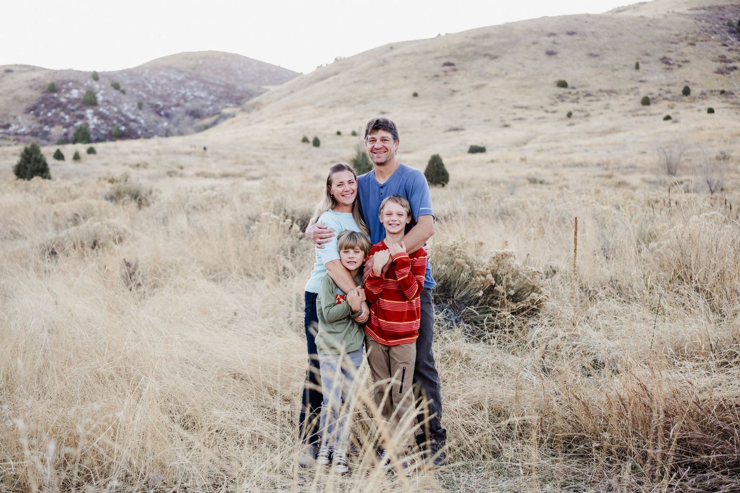Golden Colorado family photographer captures a smiling family surrounded by warm grasses and foothill views at Matthews / Winter Park.