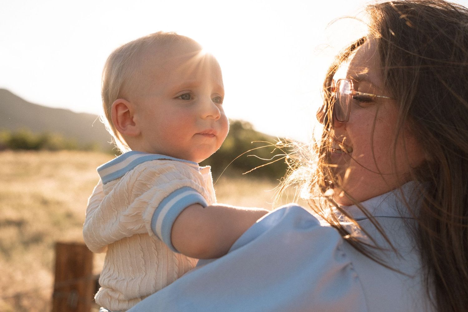 Mother holding young son, backlight by golden sun flare at South Valley Park in Littleton, Colorado during family photo session.