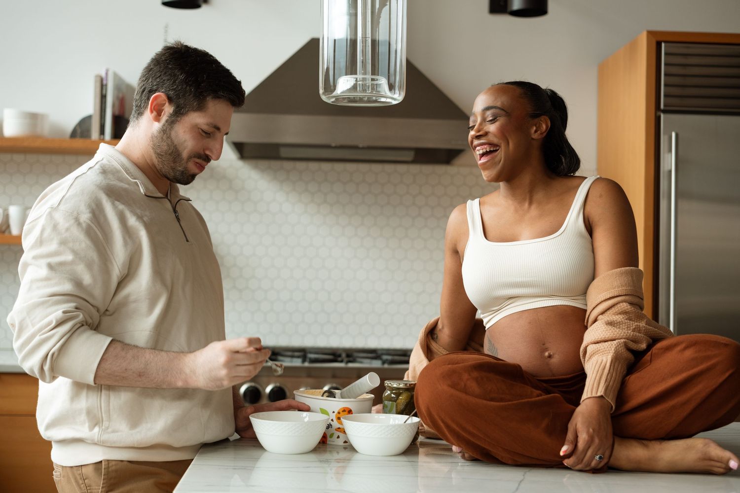 Mother sitting on counter, laughing, as father-to-be scoops ice cream.