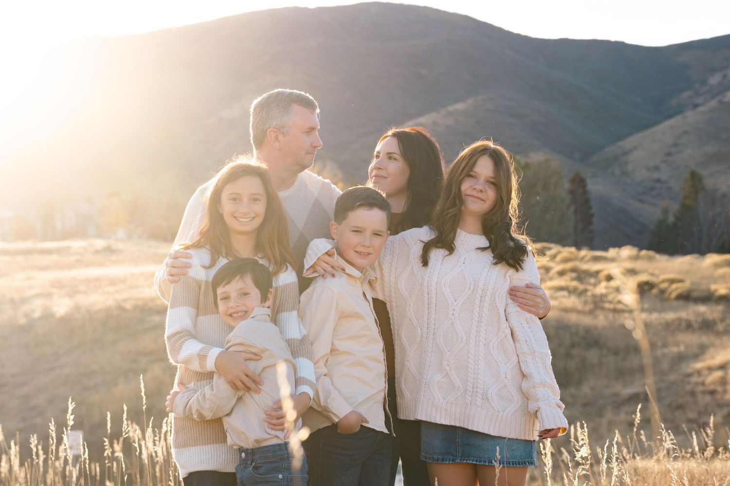 Denver family standing close together, tall grasses in foreground, foothills in background.