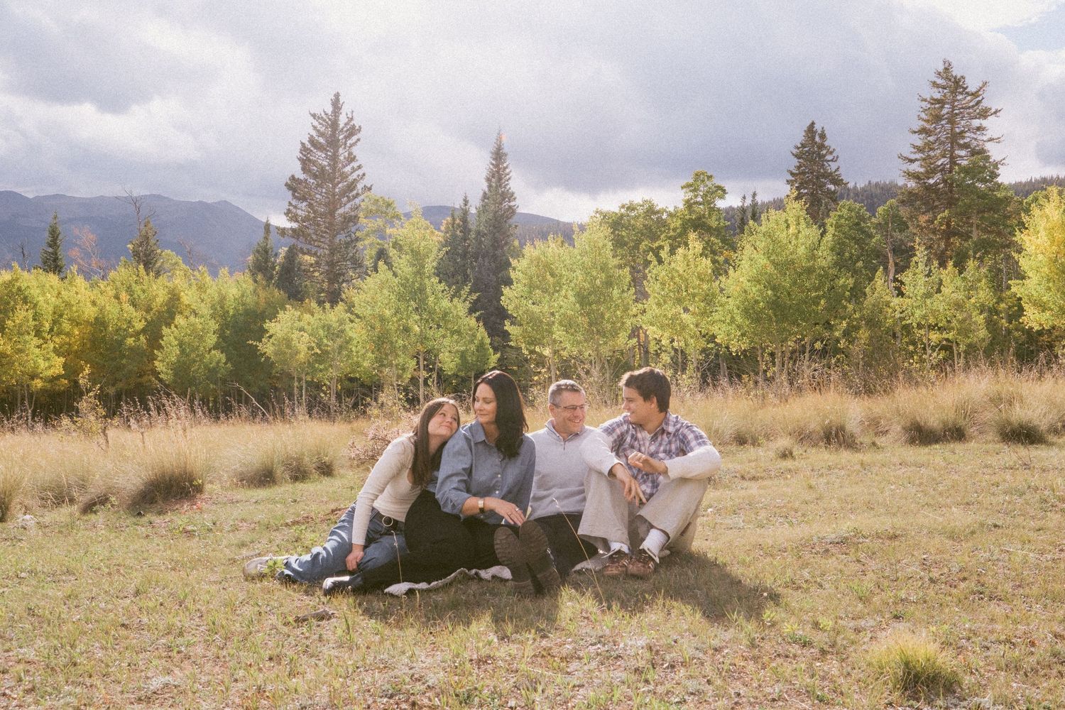 Family with teenagers in Colorado mountains, evergreens, aspens, mountains and moody skies in background.