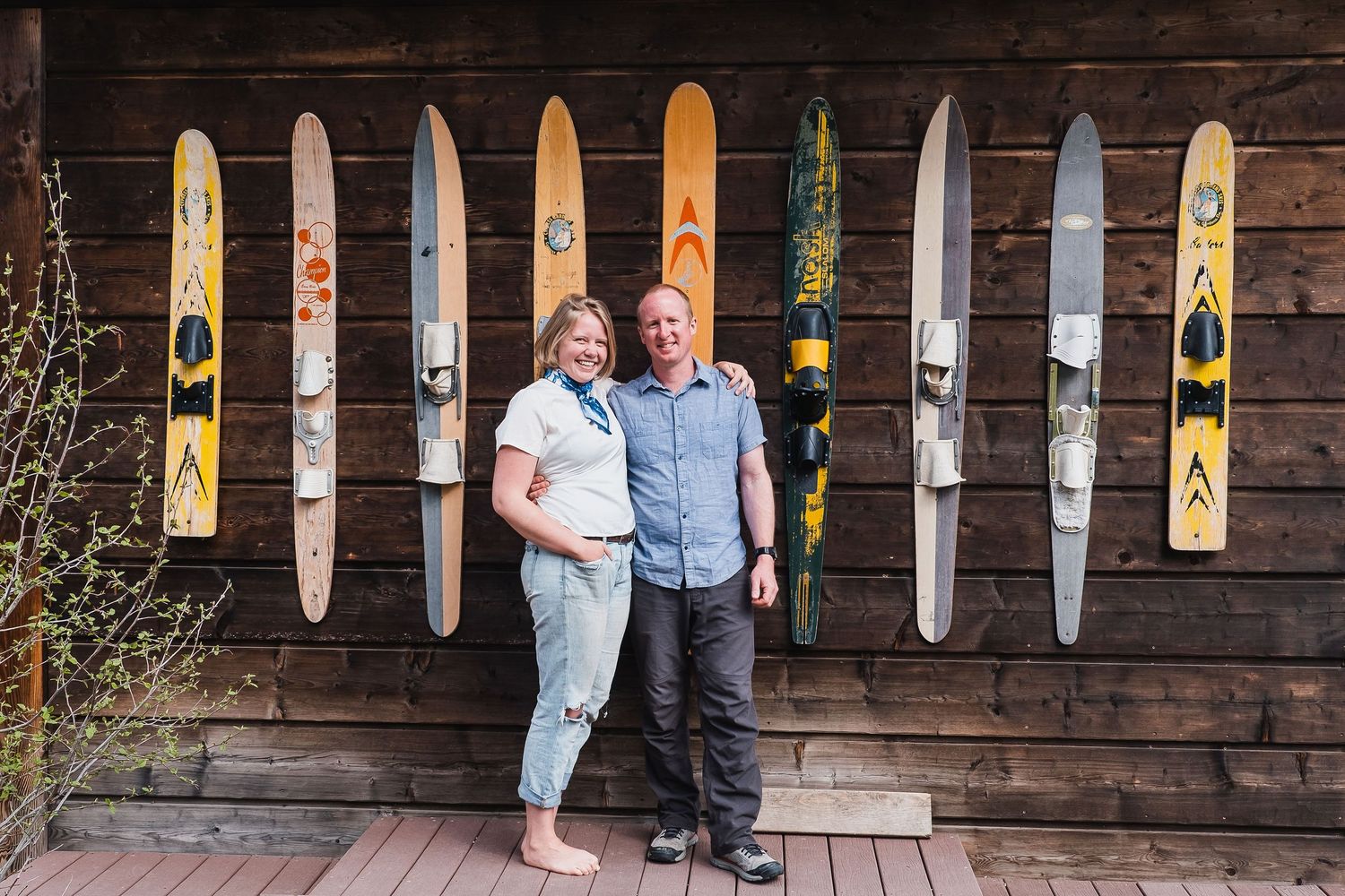 Young couple standing together, smiling, in front of boathouse affixed with colorful waterskis.