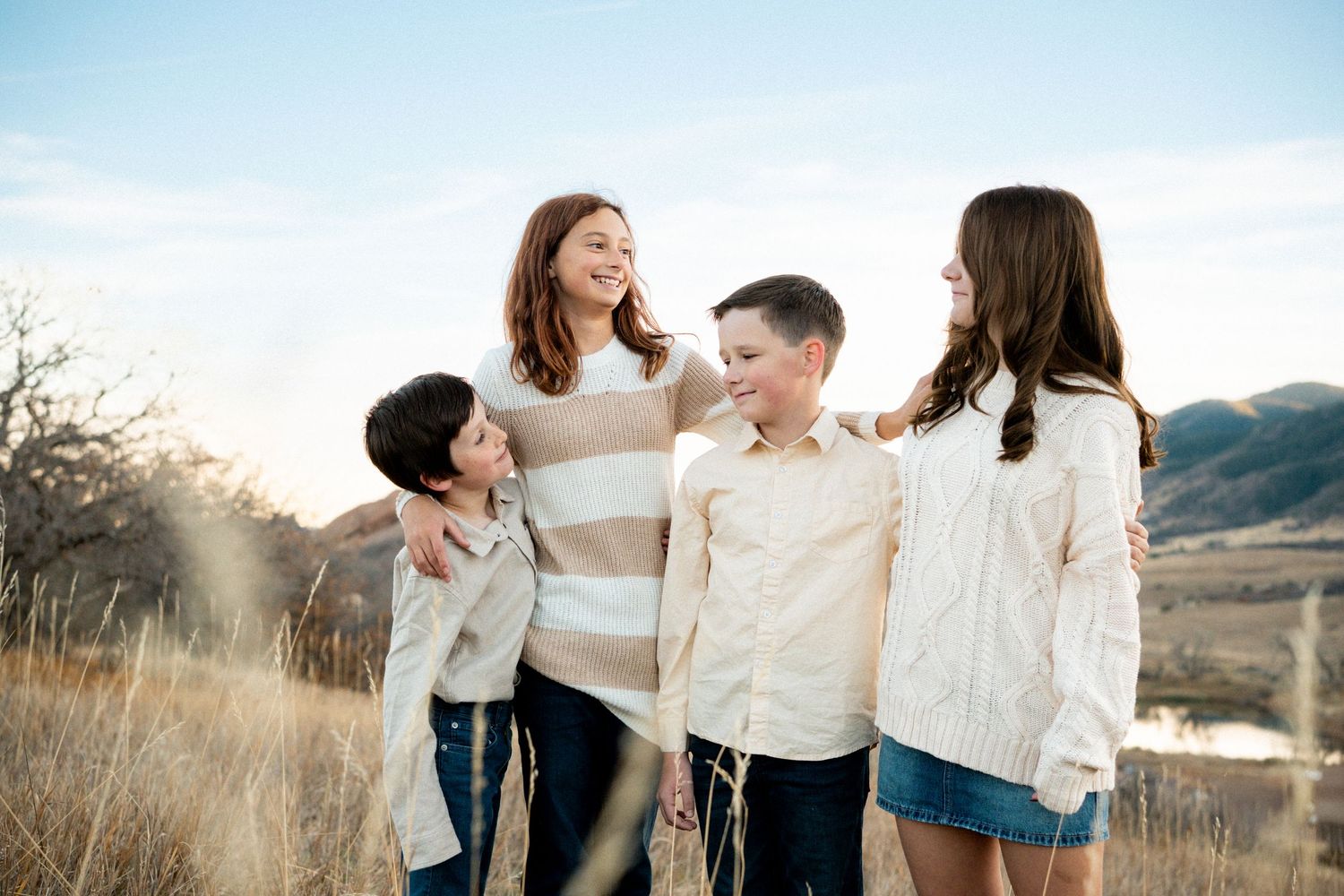 Portrait of blended siblings standing together, smiling and laughing toward one another.