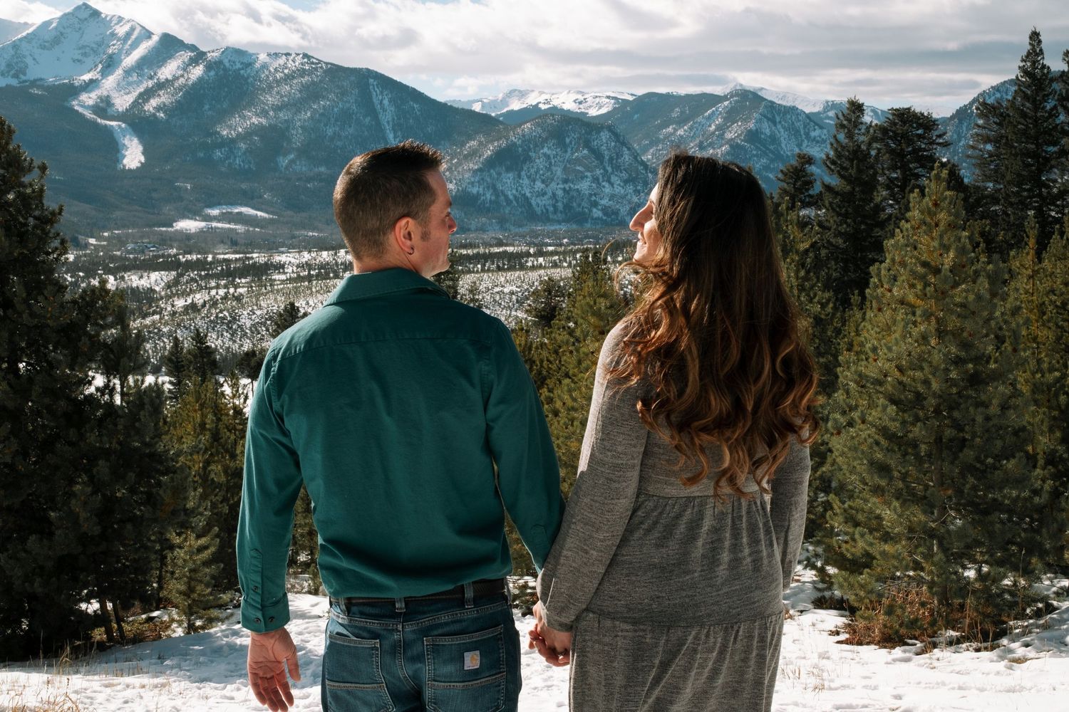 Couple looking at one another, dramatic mountains in the background, during engagement photo session at Sapphire Point Overlook.