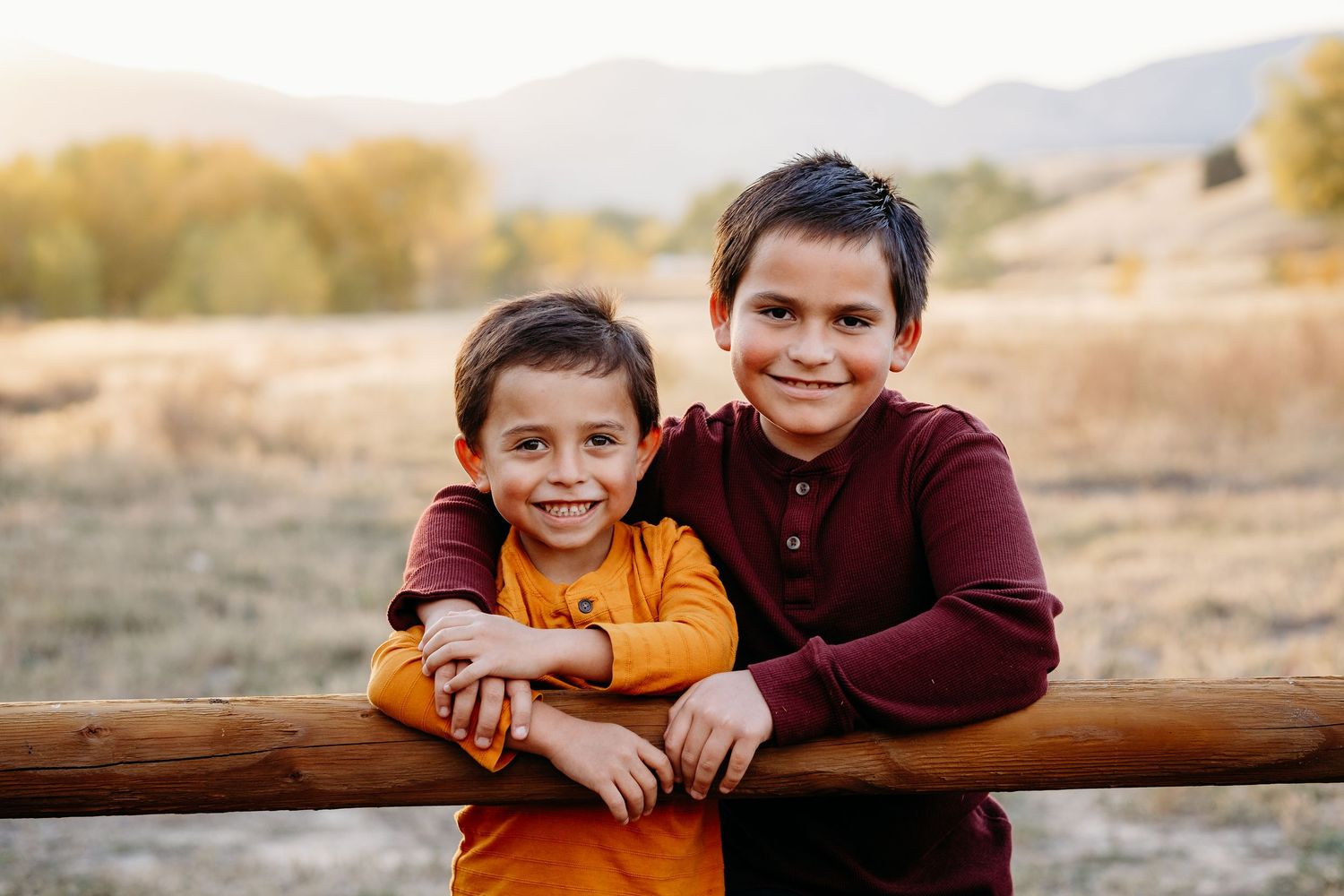 Two young brothers, one with his hand around the other, both smiling at the camera, Colorado foothills in the background.