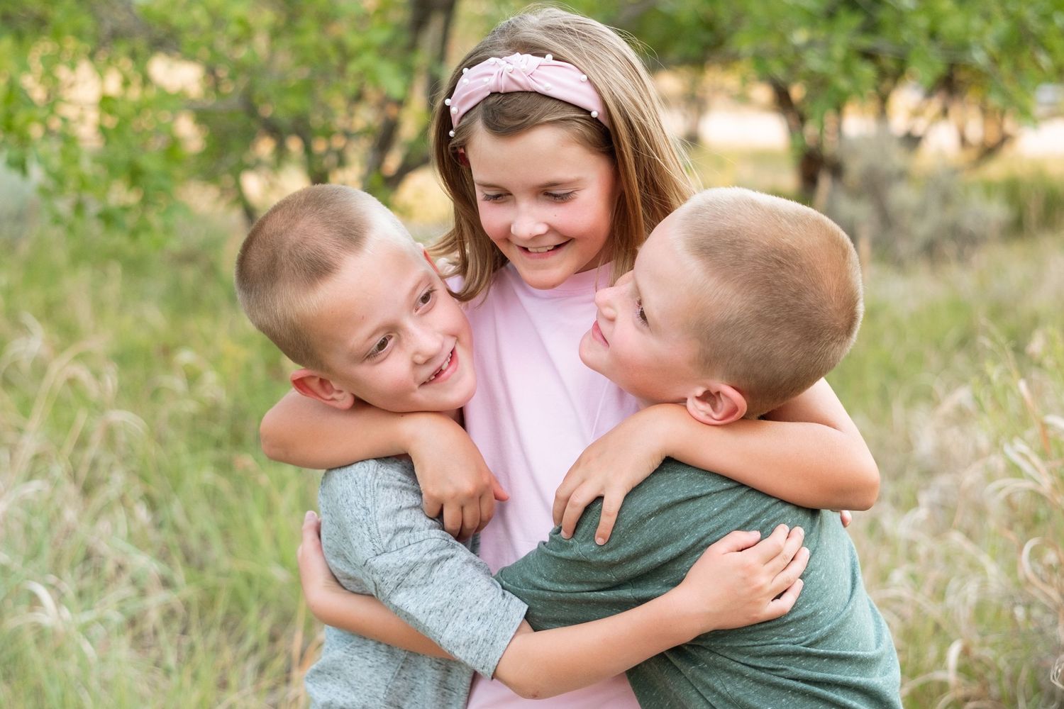 Older sister hugging twin brothers tightly.