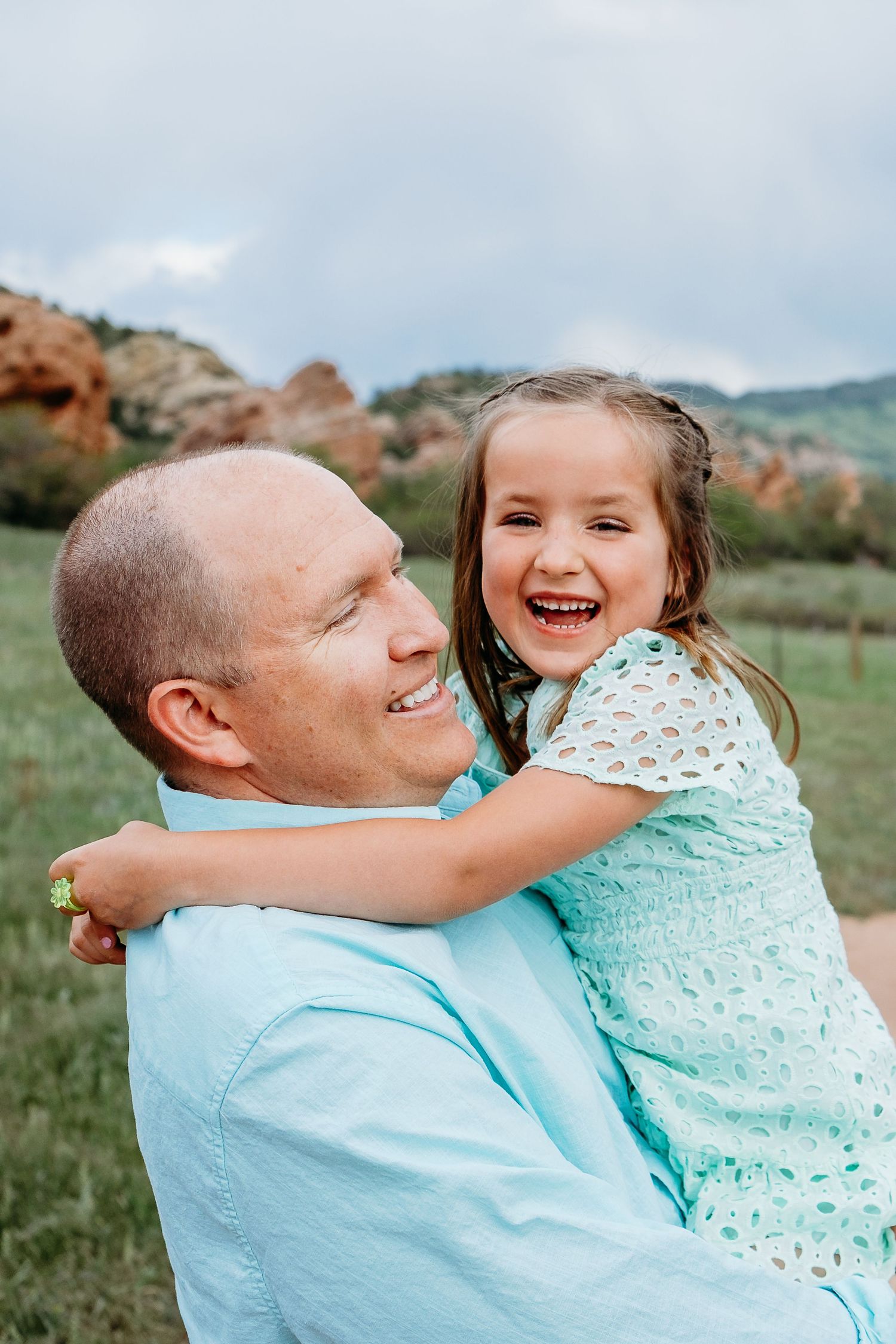 Father holding smiling daughter, South Valley Park rock formations in background.
