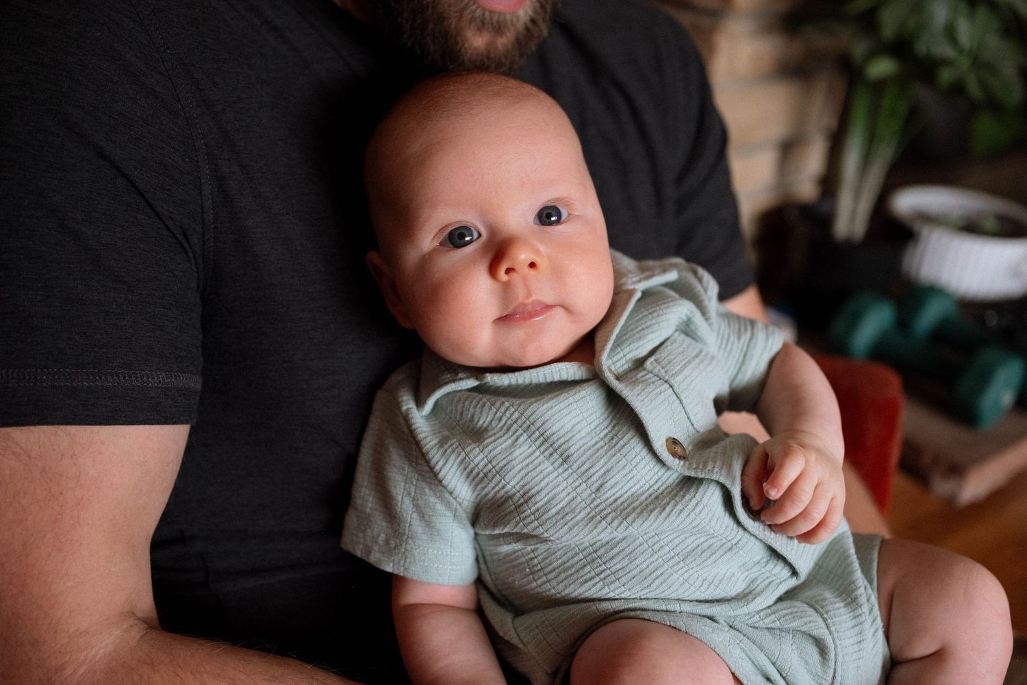 Baby peering into camera, while being held by father.
