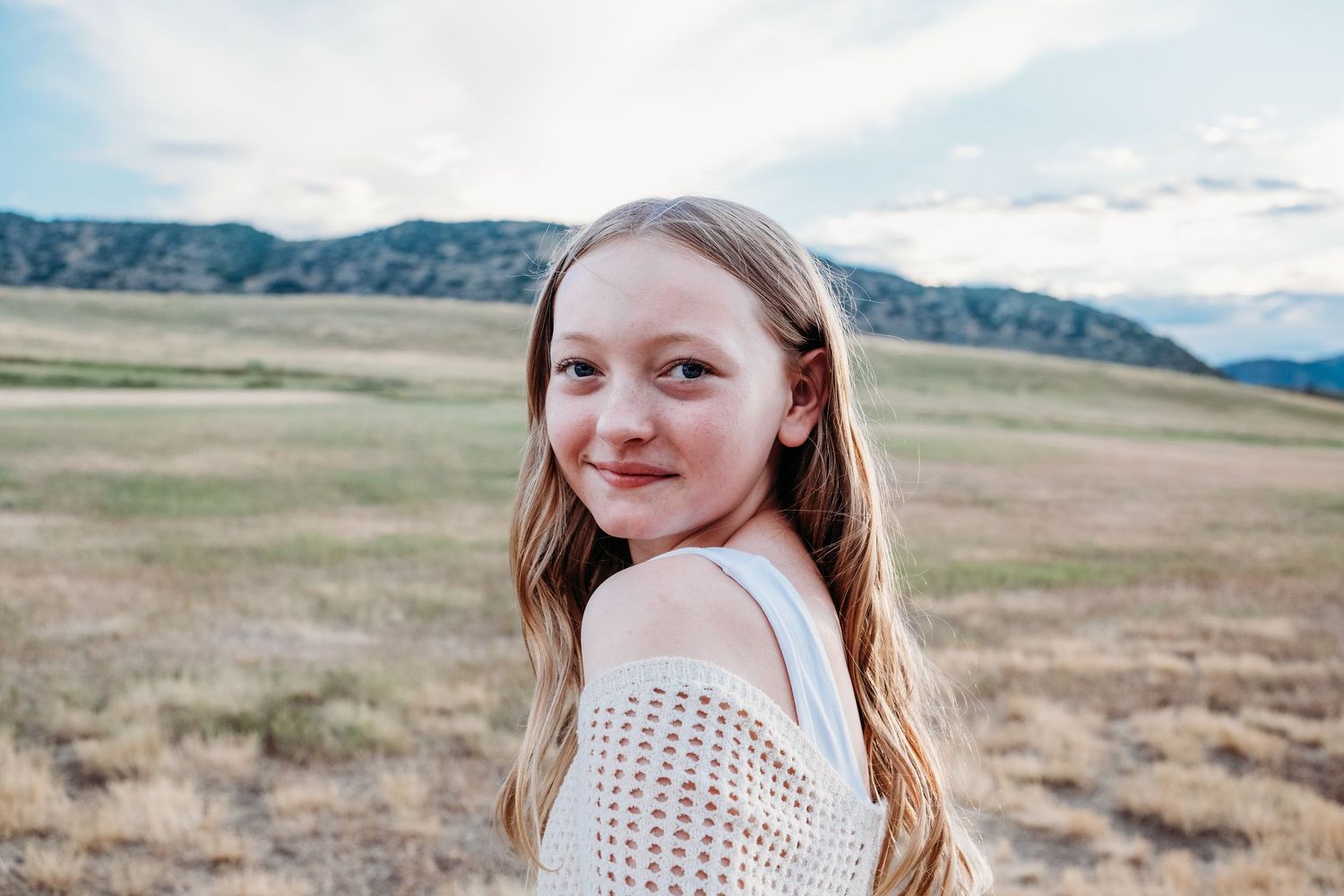 Smiling pre-teen girl with long hair, photographed at Hildebrand Ranch Park in Littleton, CO, with foothills and open field in the backgroun
