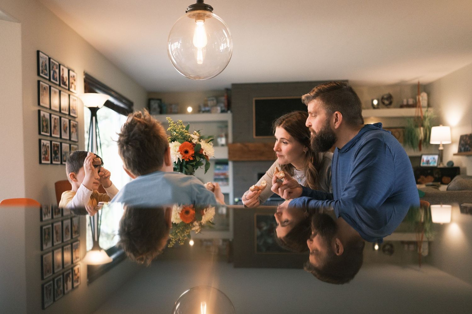 Family eating donuts at a living room table, their reflections in the black counter top below them.