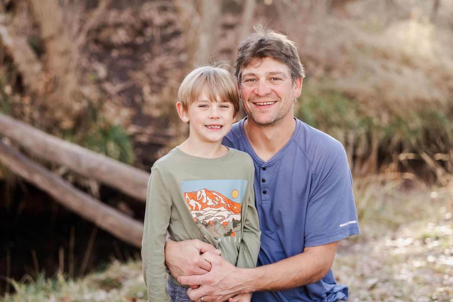 Father and son smiling, near river in Golden, Colorado during family photo session.