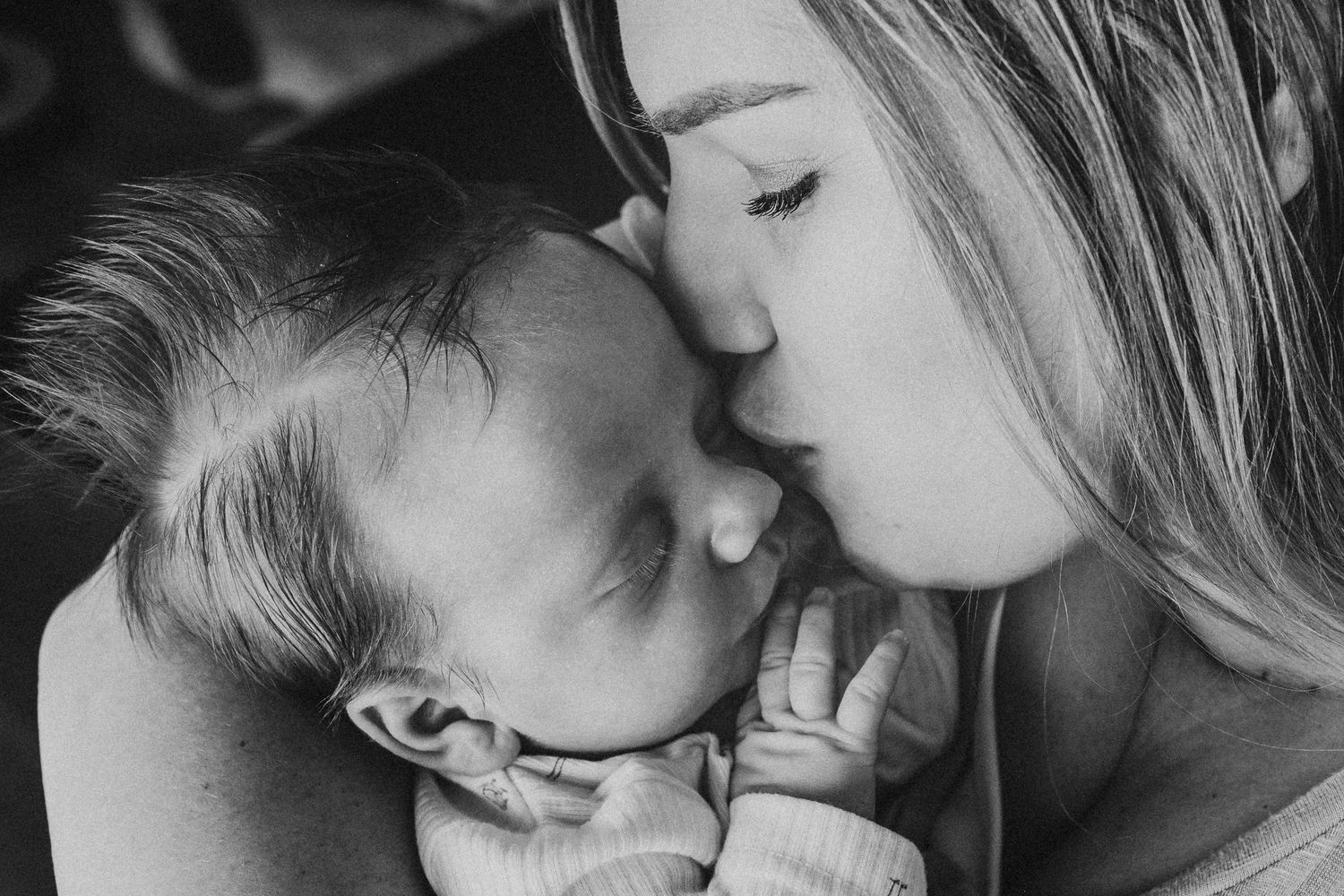 Close up black and white of mother kissing newborn son on the cheek.