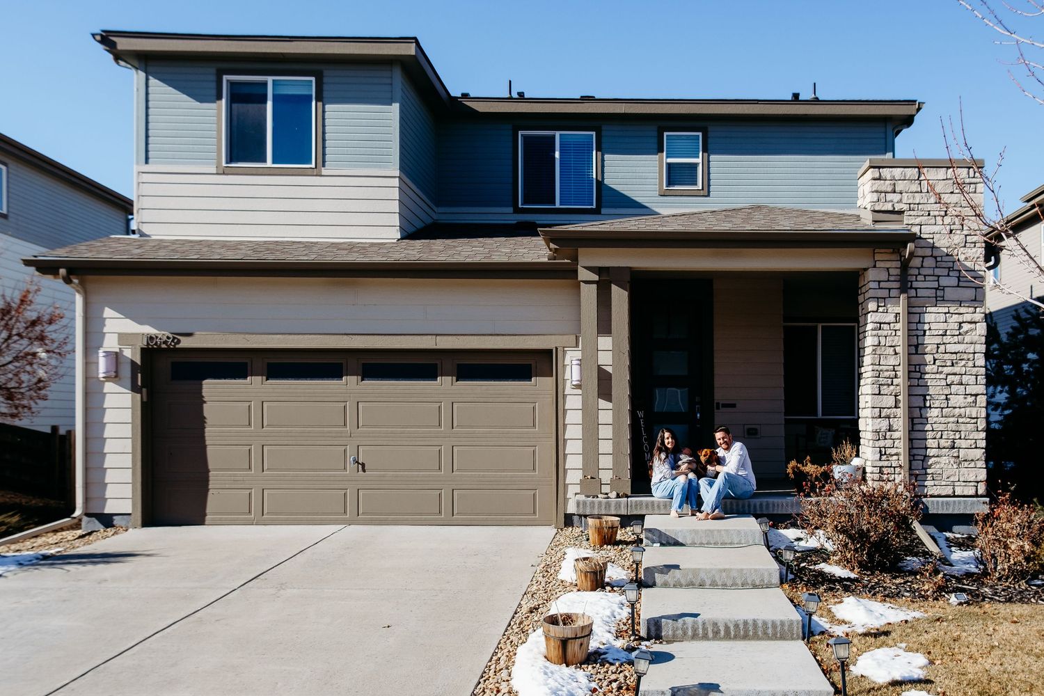 Mother, father, baby and dog sitting outside of modern home in Reunion, Commerce City, Colorado.