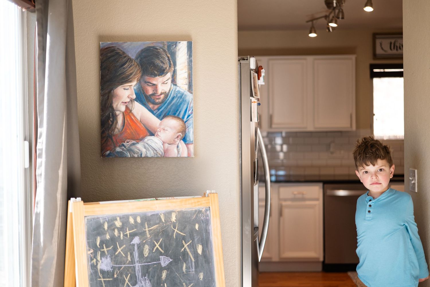 Boy standing next to a painting of him as a baby and parents holding him.