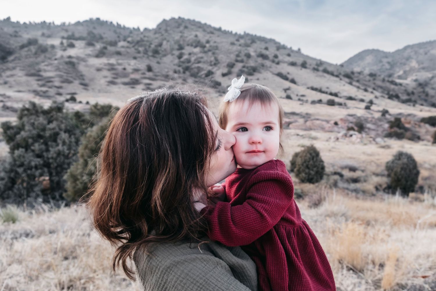 Mother kissing baby's cheek, foothills in the background at Mount Falcon East.