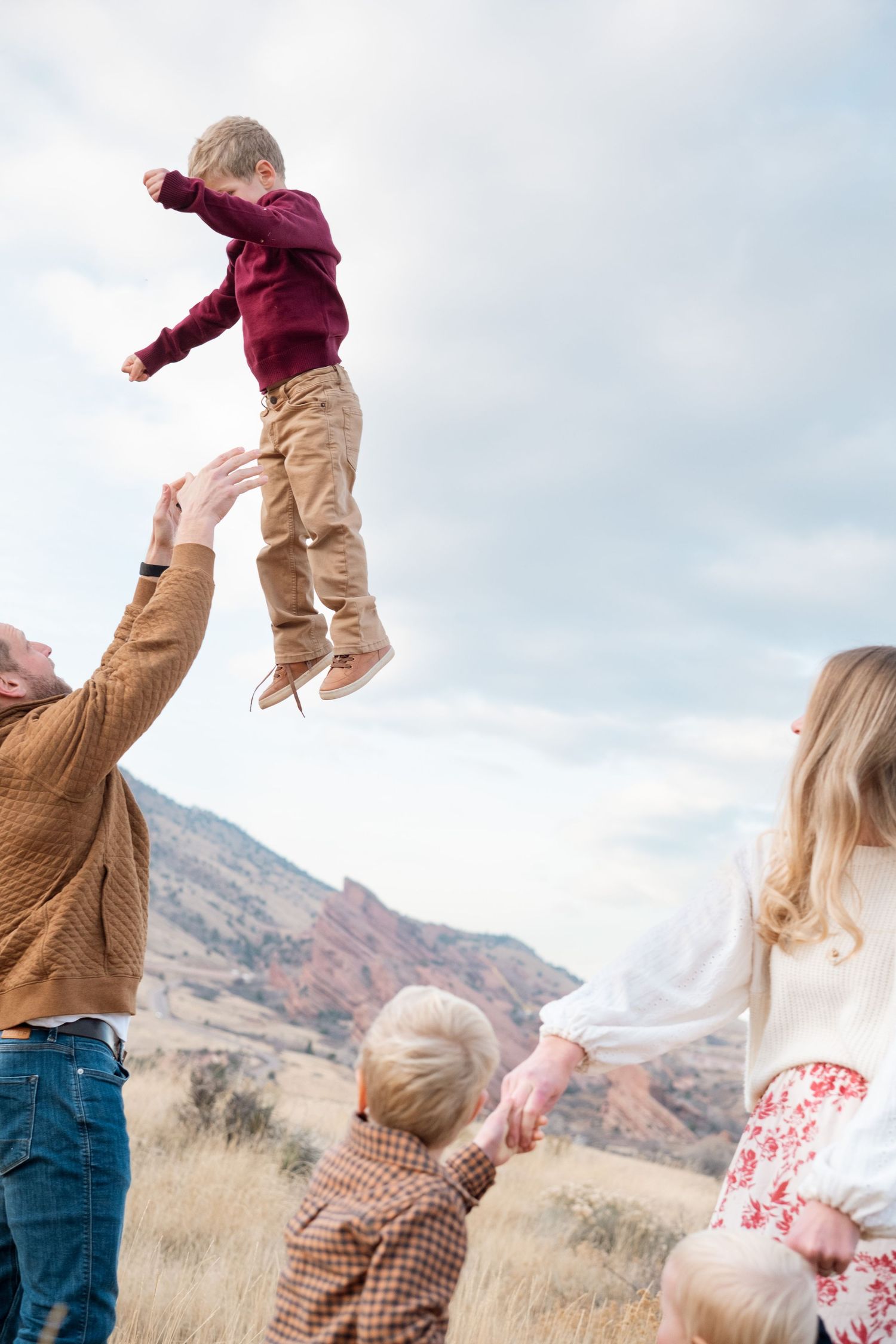 Father playfully tossing son in the air as mother and two sons stand in foreground, watching.