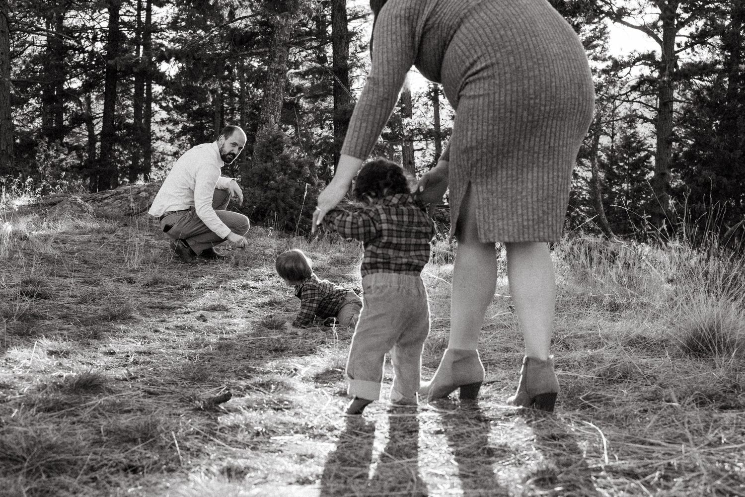 Black and white portrait of mother holding one year old's hands as he walks toward his twin and father int he mountains at Mt Falcon West.