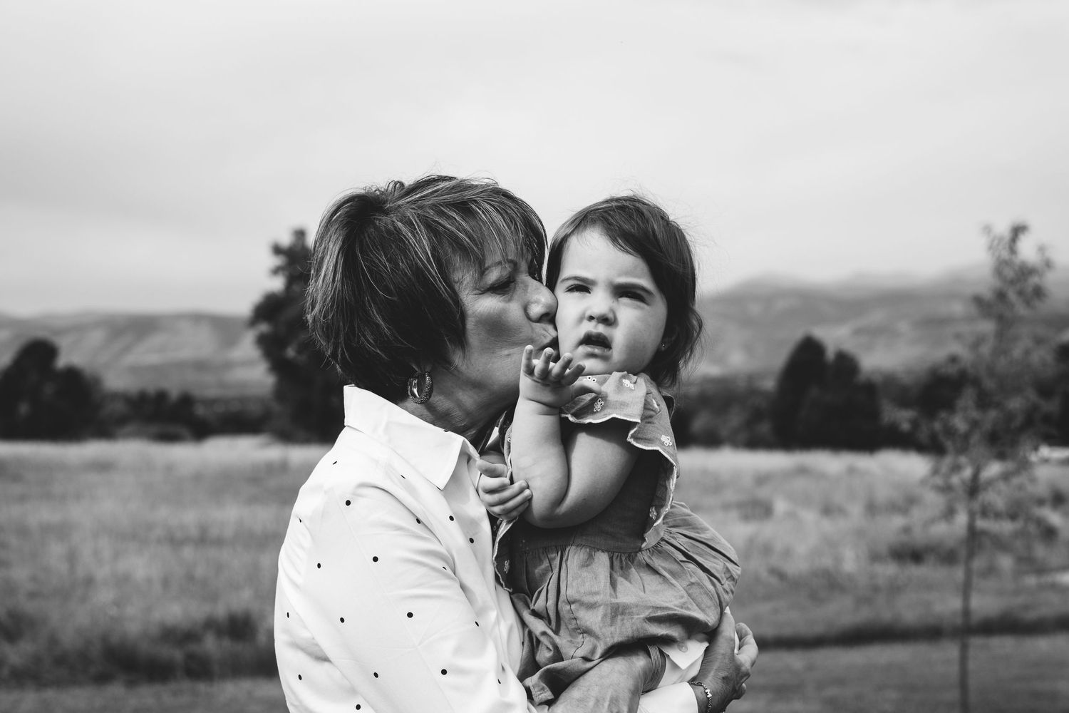 Captivating black and white portrait of grandmother kissing toddler girl on cheek.