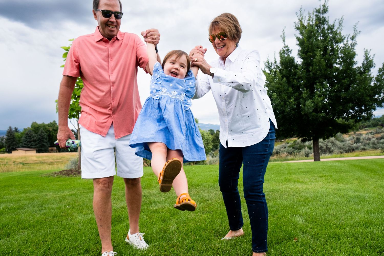 Grandparents playfully swinging toddler girl in the air, girl laughing.