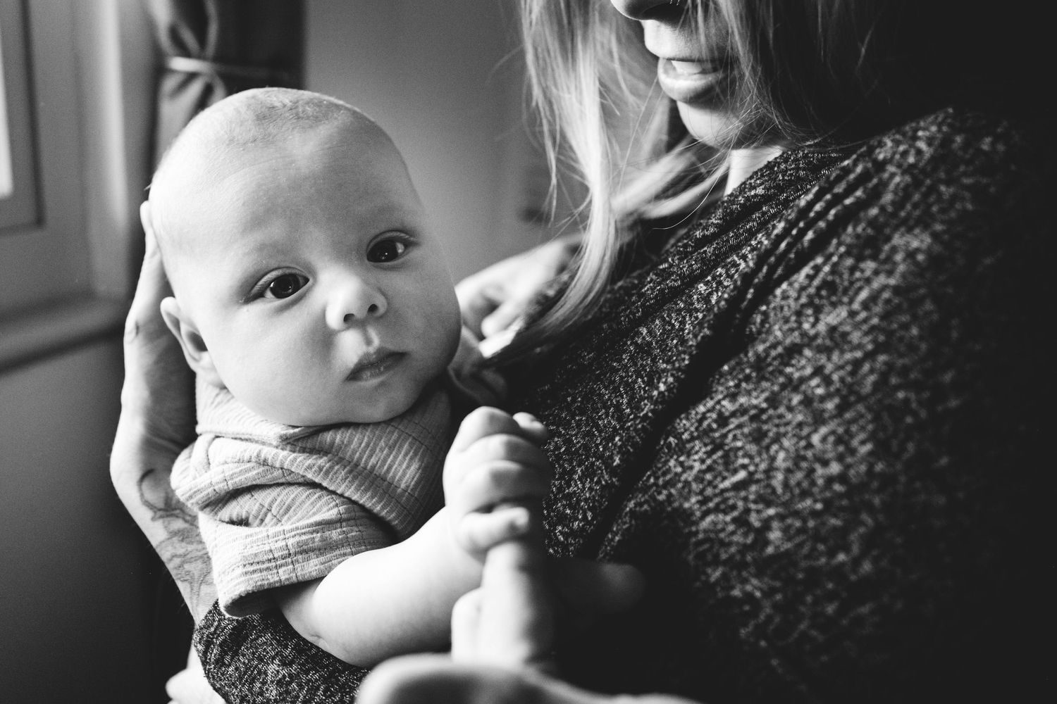 Black and white close up of baby being held by mother, baby holding on to father's index finger.