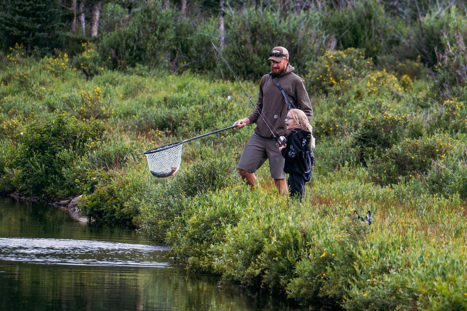 Father and daughter fishing at pond in mountains of Colorado.