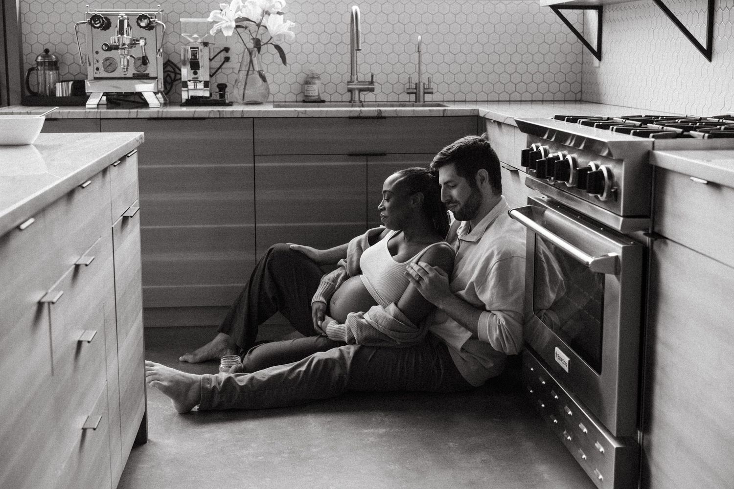 Pregnant couple snuggling on the floor of modern kitchen.