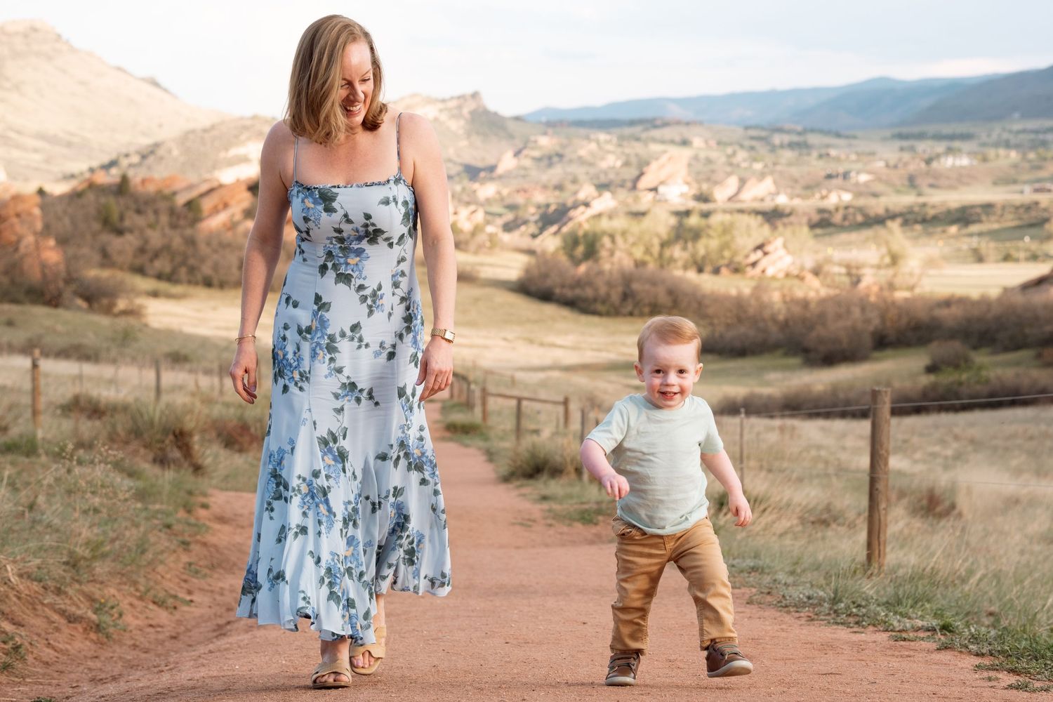 Mother walking next to toddler boy walking toward camera, smiling.