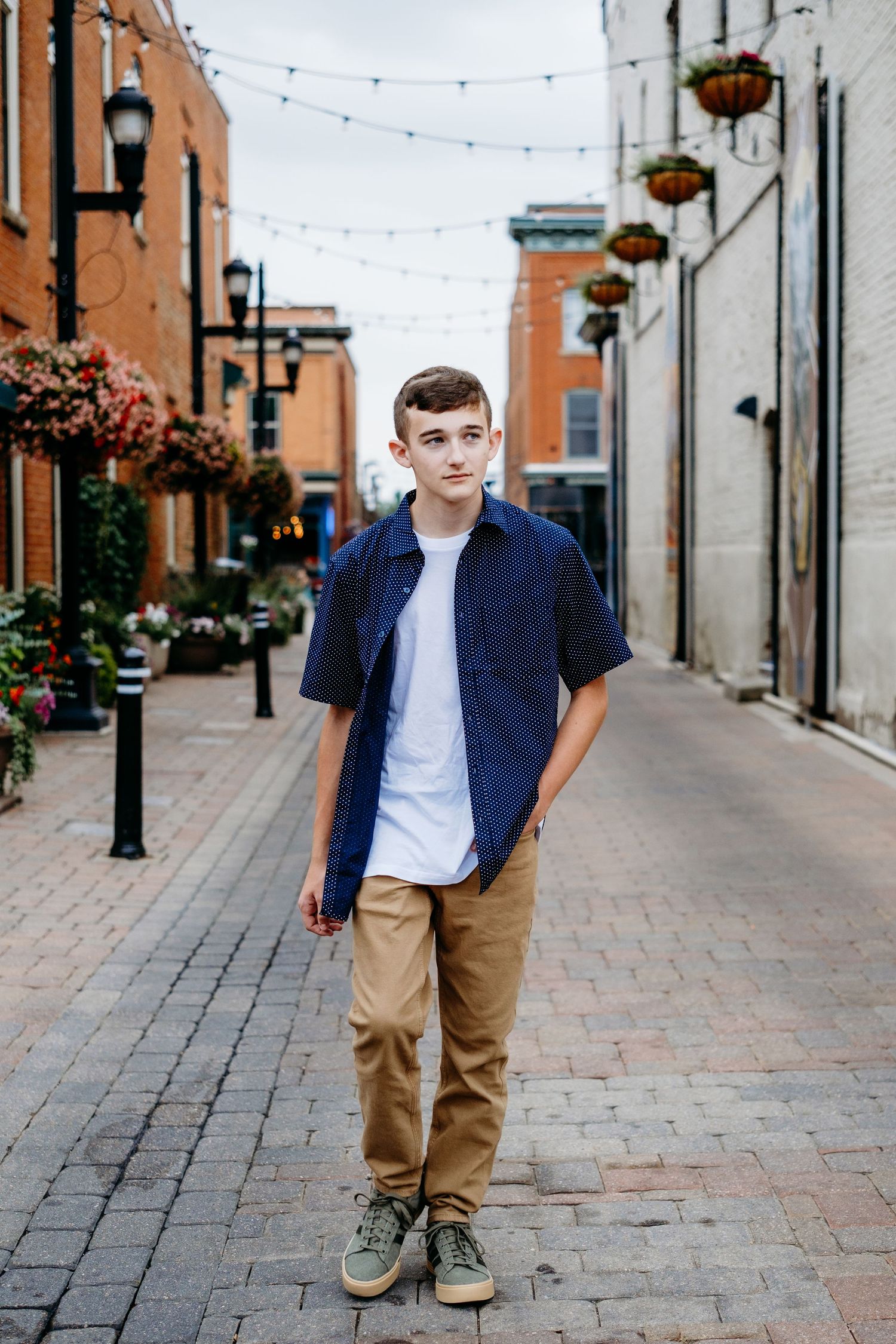 Senior portrait of a teen boy walking through a charming alley in downtown Fort Collins, featuring brick buildings and hanging plants