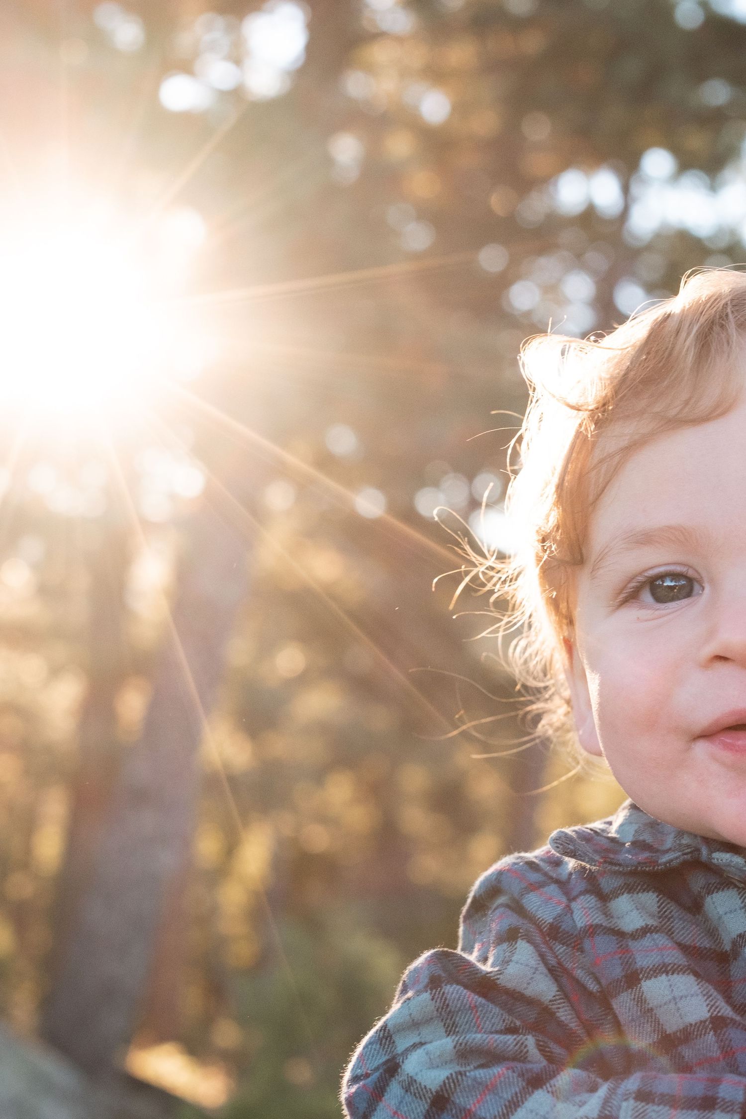 One year old twin smiling, sun flare bursting through trees in the background.