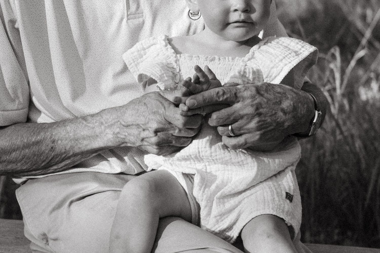 Black and white close up of grandfather holding granddaughter with focus on their hands.