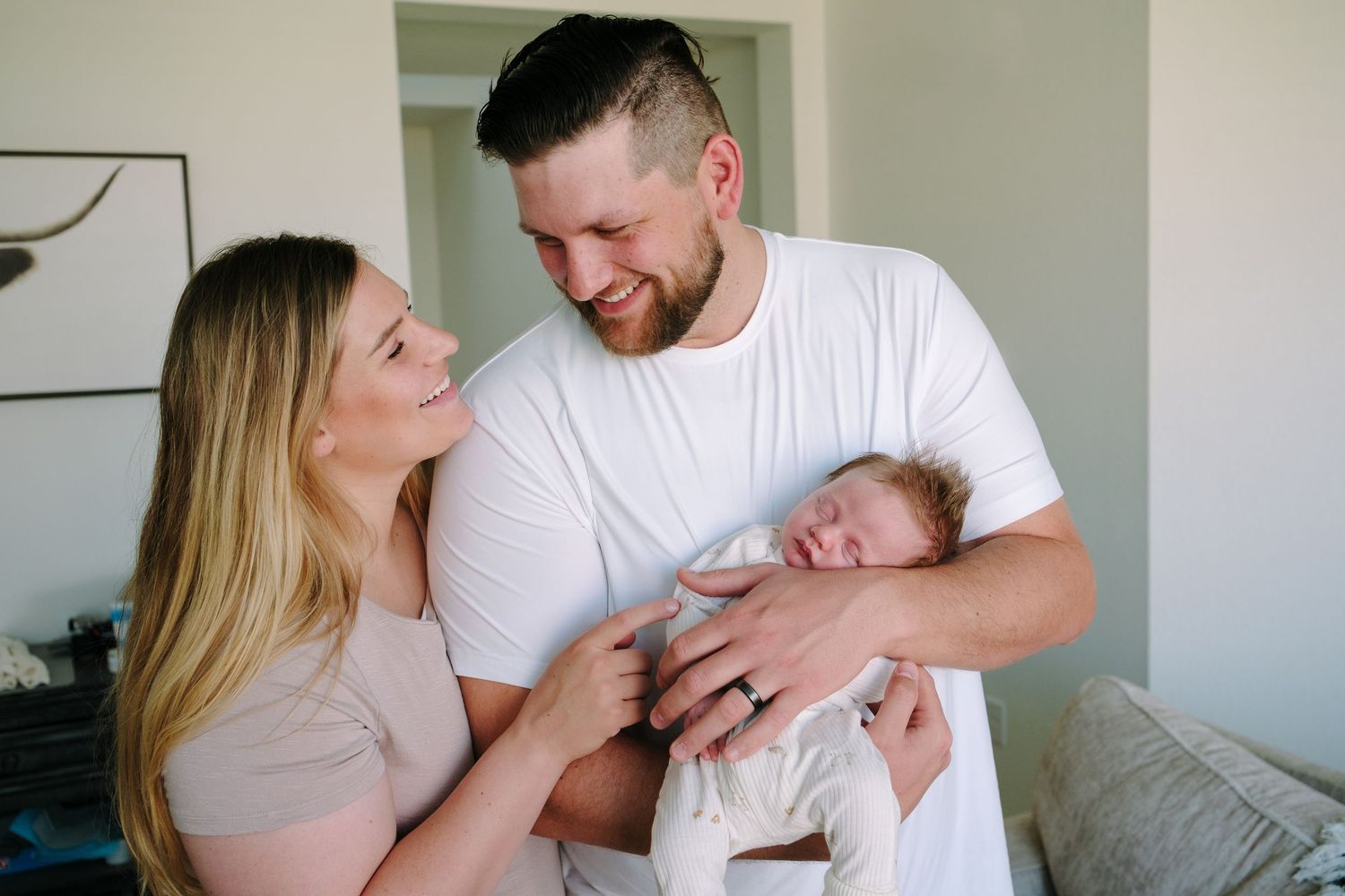Father holding newborn baby, mother snuggled to father, father and mother smiling at one another.