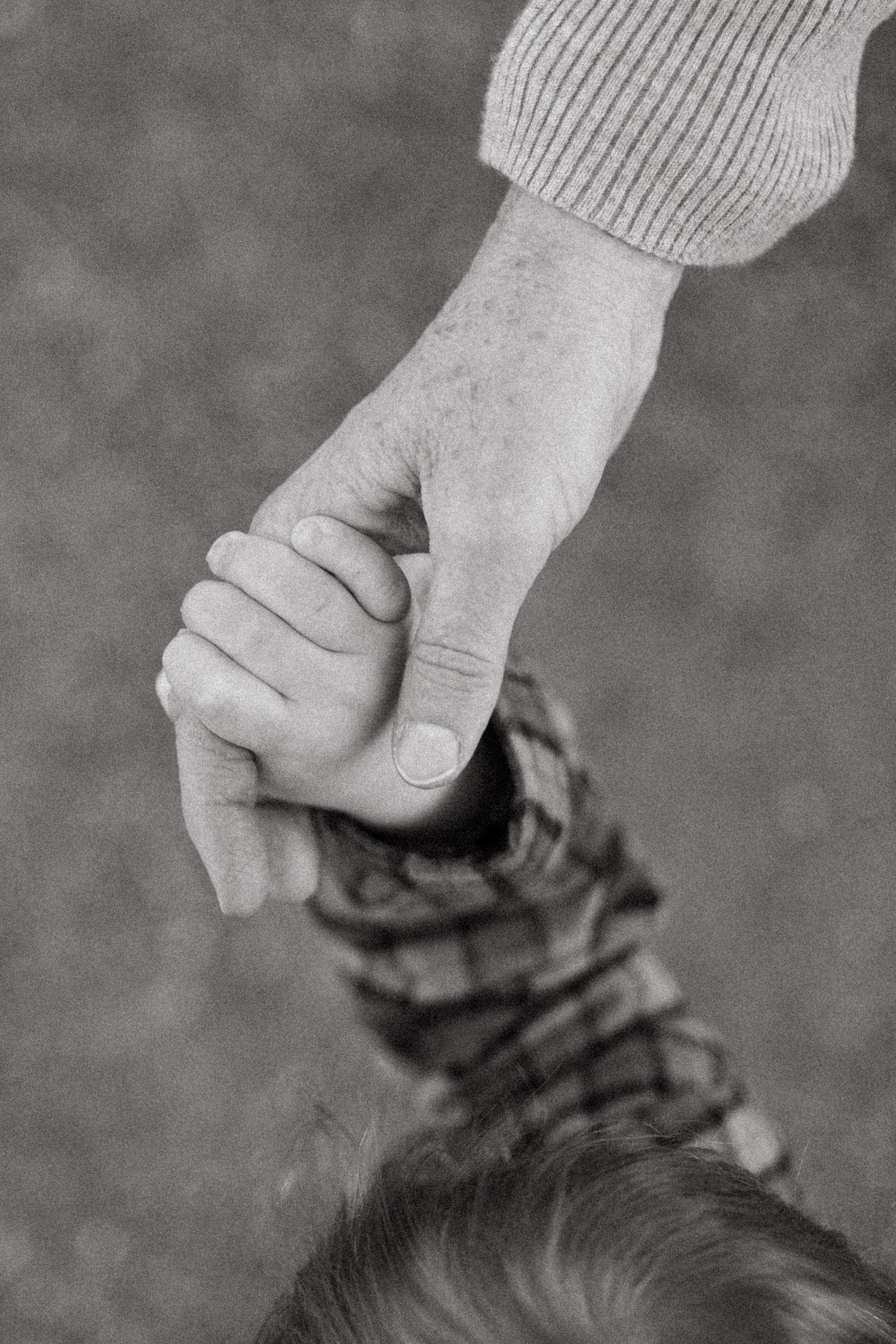 Black and white of grandma holding one year old grandson's hand.