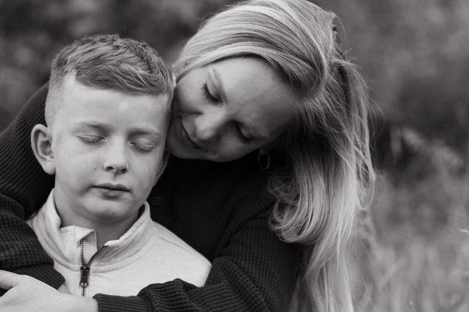 Black and white portrait of mother embracing son, both with eyes closed.