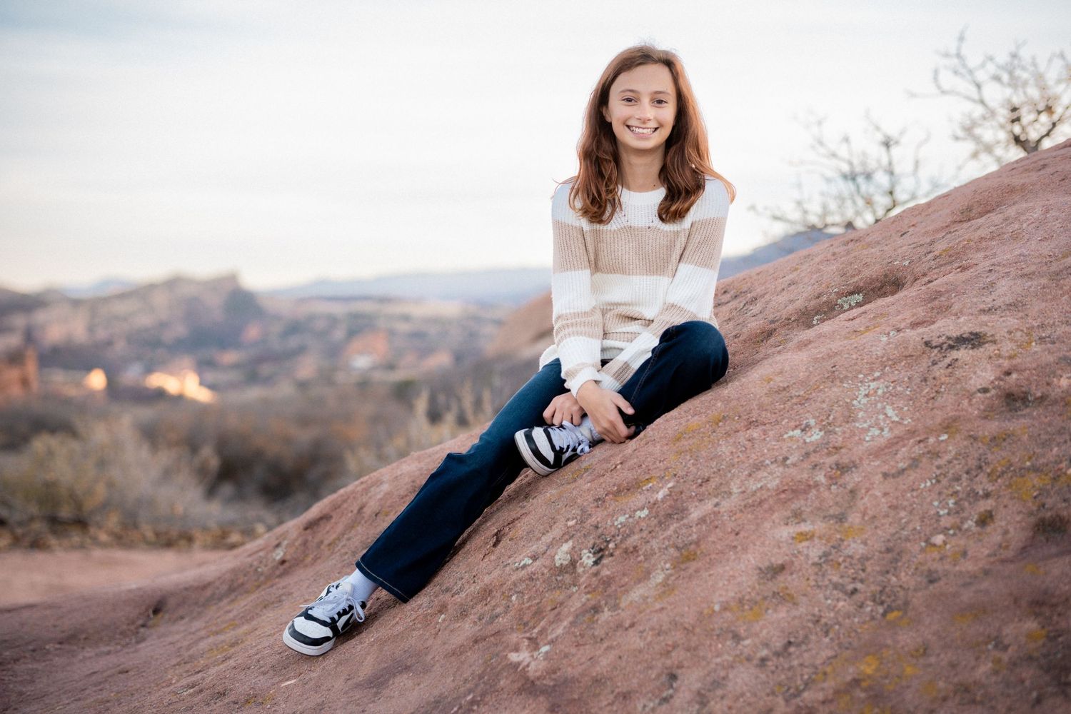 Young girl perched on rock formation, foothills in the background.