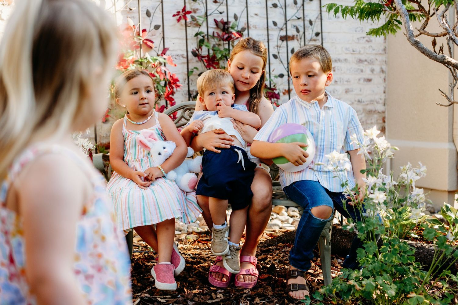 Four young cousins of various ages sitting in beautiful backyard garden, one toddler in foreground.
